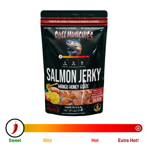 Packaging for Bull Munchies’ Mango Honey Glaze wild-caught salmon jerky. The design features a large, vibrant illustration of a leaping salmon on a red and black background. The text highlights ‘Mango Honey Glaze’ in bold letters, along with labels such as ‘No Added Hormones’ and ‘Wild-Caught Salmon Jerky.’ The bottom section includes a close-up view of the jerky pieces inside the bag, showcasing the product’s texture and color. Net weight is listed as 2.0 oz. (74 g).